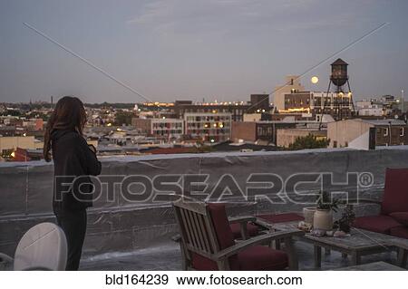 Stock Photo - Caucasian woman admiring cityscape from urban rooftop. Fotosearch