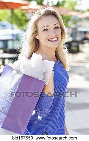 Stock Image - Caucasian woman carrying shopping bag outdoors. Fotosearch
