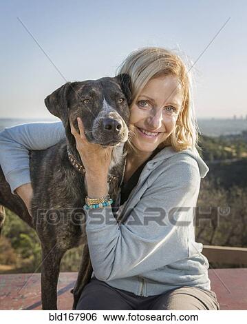 Stock Photograph - Caucasian woman hugging dog on hilltop. Fotosearch