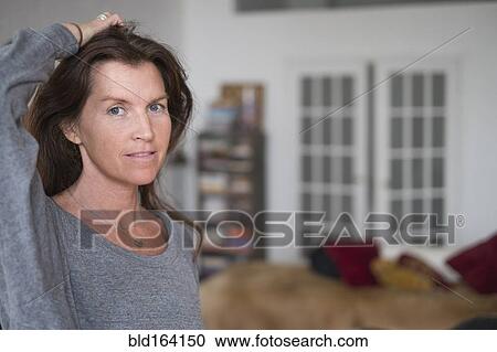 Stock Image - Caucasian woman in living room with hand in hair. Fotosearch