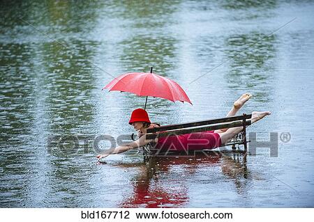 Stock Image - Caucasian woman laying on bench in flood. Fotosearch