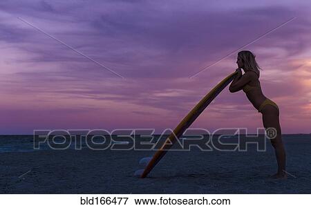 Stock Photo - Caucasian woman leaning on surfboard on beach. Fotosearch