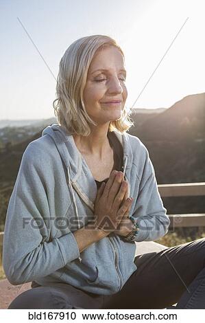 Stock Image - Caucasian woman meditating on hilltop. Fotosearch