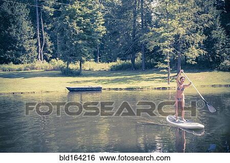 Stock Photograph - Caucasian woman paddleboarding in lake. Fotosearch