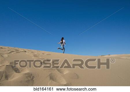 Stock Image - Caucasian woman running on sand dune. Fotosearch