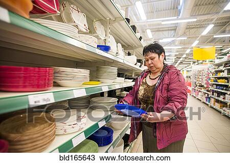 Stock Image - Caucasian woman shopping for dishes in store. Fotosearch