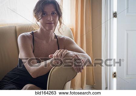 Stock Image - Caucasian woman sitting in armchair in living room. Fotosearch