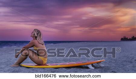 Stock Photograph - Caucasian woman sitting on surfboard on beach. Fotosearch