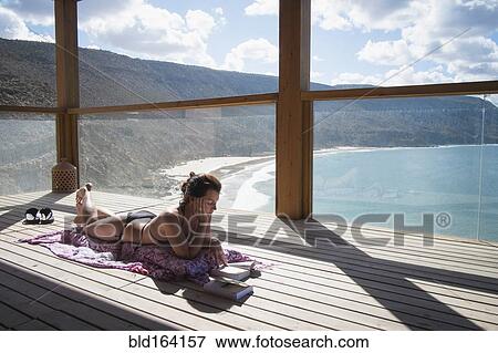 Stock Photo - Caucasian woman sunbathing on deck over beach. Fotosearch