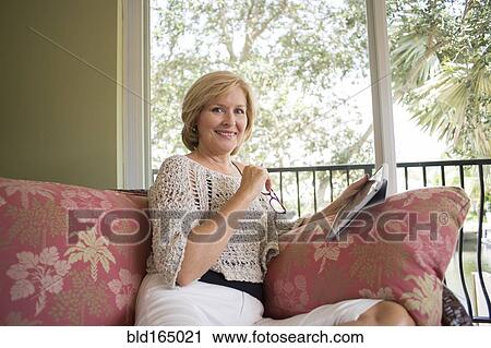 Stock Image - Caucasian woman using digital tablet on sofa. Fotosearch