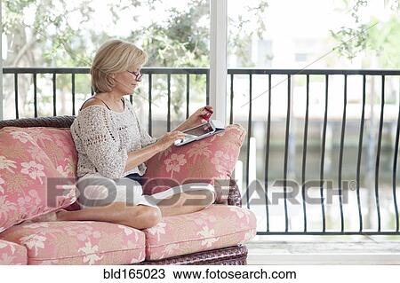 Stock Image - Caucasian woman using digital tablet on sofa. Fotosearch