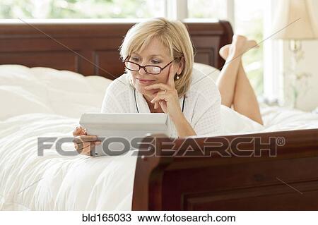 Stock Image - Caucasian woman using digital tablet on bed. Fotosearch