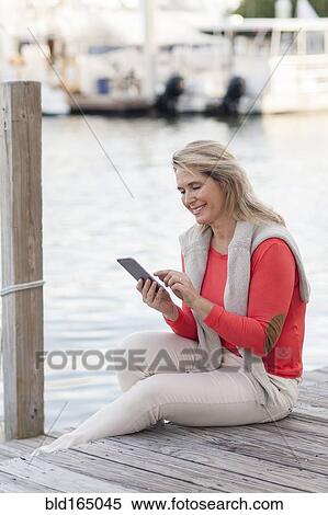 Stock Photography - Caucasian woman using digital tablet on harbor dock. Fotosearch