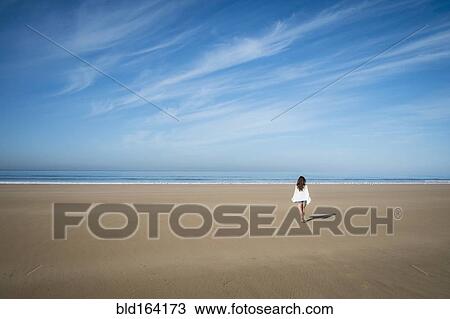 Stock Image - Caucasian woman walking on beach under blue sky. Fotosearch