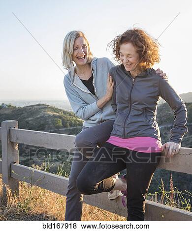 Stock Photo - Caucasian women sitting on fence on hilltop. Fotosearch