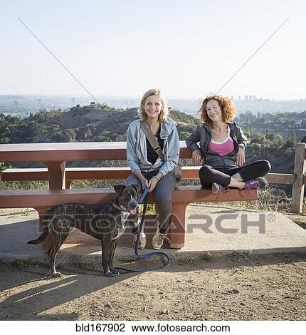 Stock Image - Caucasian women sitting with dog on hilltop. Fotosearch
