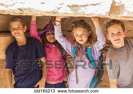 Stock Image - Children crouching under rock formation. Fotosearch