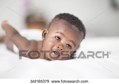 Stock Photo - Close up of Black baby laying on bed. Fotosearch