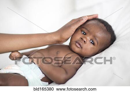 Stock Image - Close up of Black mother patting baby on bed. Fotosearch