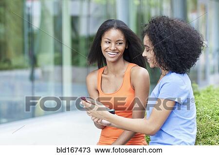 Stock Image - Close up of Black women using cell phone outdoors. Fotosearch