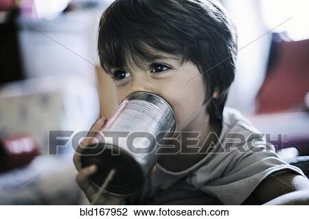 Stock Image - Close up of boy playing with tin can telephone. Fotosearch