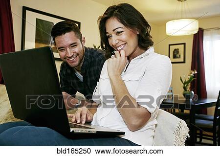 Stock Image - Close up of couple using laptop on sofa. Fotosearch