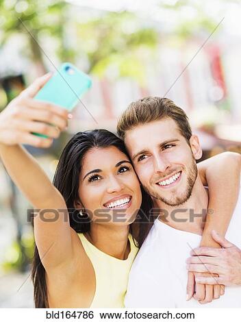 Stock Photograph - Close up of Hispanic couple taking selfie outdoors. Fotosearch