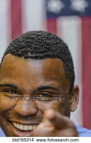 Picture - Close up of smiling Black man pointing in front of American flag. Fotosearch
