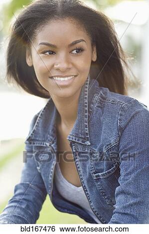 Stock Photograph - Close up of smiling Black woman sitting outdoors. Fotosearch