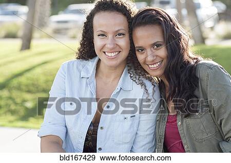 Stock Photo - Close up of smiling women hugging in park. Fotosearch