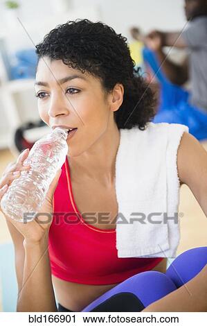 Close up of woman drinking water bottle in gym View Large Photo Image Stock Image - Close up of woman drinking water bottle in gym. Fotosearch