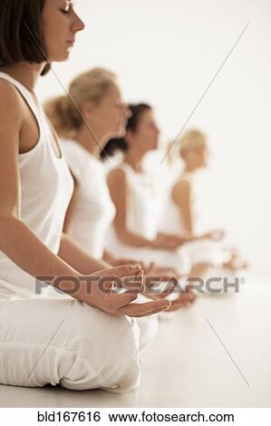 Stock Photograph - Close up of women meditating in yoga class. Fotosearch