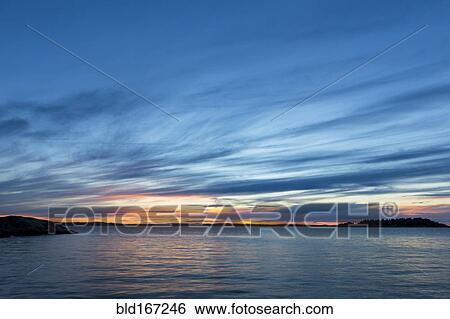 Stock Photograph - Clouds in sunset sky over still ocean. Fotosearch