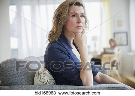 Stock Image - Concerned Caucasian woman sitting on sofa. Fotosearch