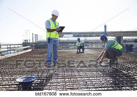 Stock Photo - Construction workers arranging rebar at construction site. Fotosearch