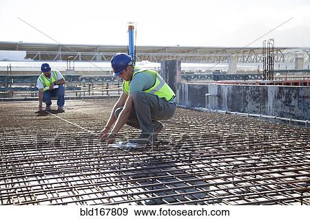 Stock Photo - Construction workers arranging rebar at construction site. Fotosearch