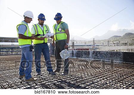 Stock Image - Construction workers talking on rebar at construction site. Fotosearch