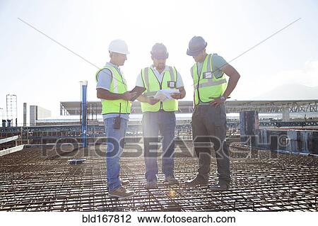 Stock Image - Construction workers talking on rebar at construction site. Fotosearch