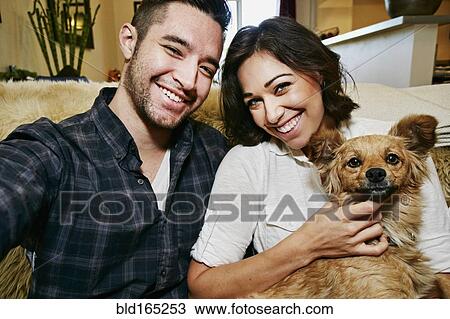 Couple holding dog on sofa in living room View Large Photo Image Stock Image - Couple holding dog on sofa in living room. Fotosearch