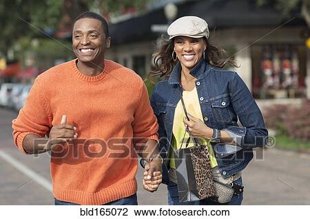 Couple holding hands and walking on sidewalk View Large Photo Image Stock Image - Couple holding hands and walking on sidewalk. Fotosearch
