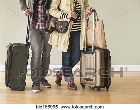Couple holding rolling luggage in living room View Large Photo Image Stock Photography - Couple holding rolling luggage in living room. Fotosearch