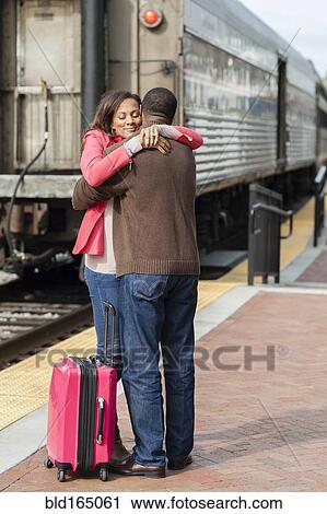 Stock Image - Couple hugging at train station. Fotosearch