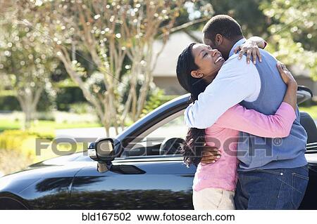 Stock Image - Couple hugging near convertible. Fotosearch
