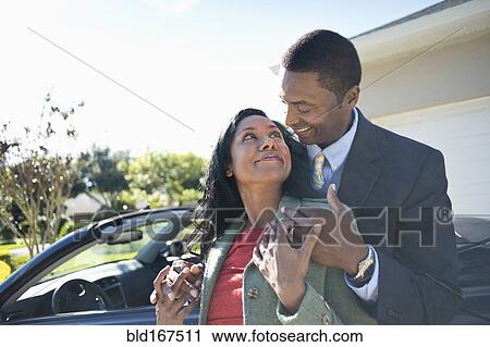 Stock Image - Couple hugging near convertible. Fotosearch