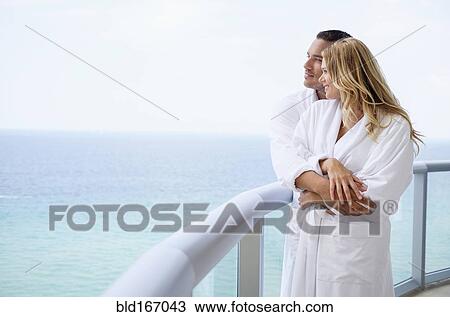 Stock Image - Couple hugging on balcony over ocean. Fotosearch
