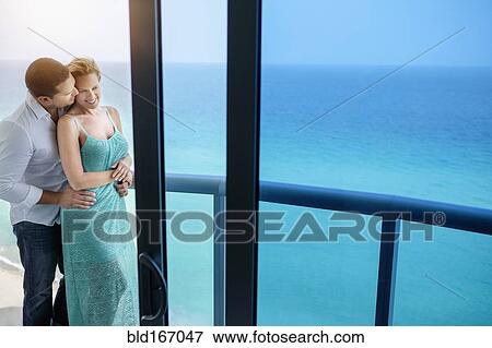 Stock Photo - Couple kissing on balcony over ocean. Fotosearch
