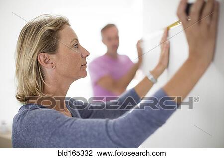 Stock Image - Couple measuring wall in new home. Fotosearch