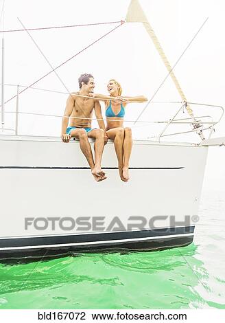 Stock Image - Couple sitting on deck of sailboat. Fotosearch