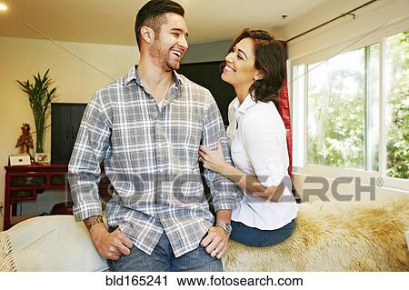 Couple smiling on sofa in living room View Large Photo Image Stock Image - Couple smiling on sofa in living room. Fotosearch