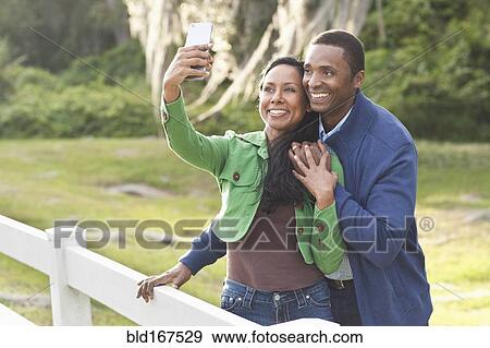 Stock Photo - Couple taking selfies at fence. Fotosearch